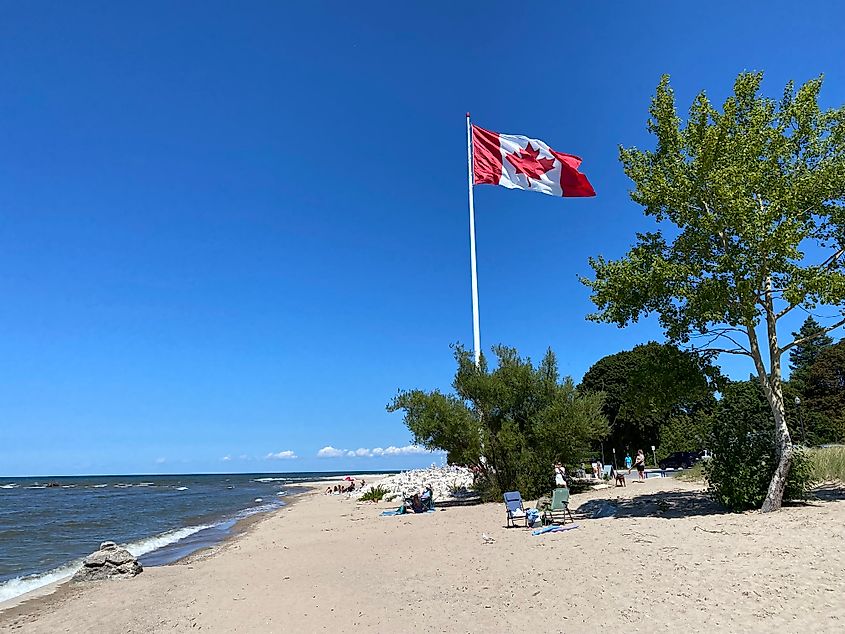 A large Canadian flag stands above a sandy lake beach.