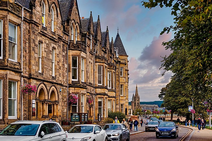 Victorian-era buildings line a busy street in Inverness, where locals and tourists stroll amid shops, traffic, and views of the Highland landscape.