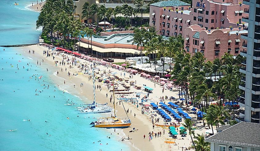 Tourists enjoying vacationing on world famous Waikiki Beach in front of the iconic Royal Hawaiian hotel in Honolulu on Oahu, Hawaii.
