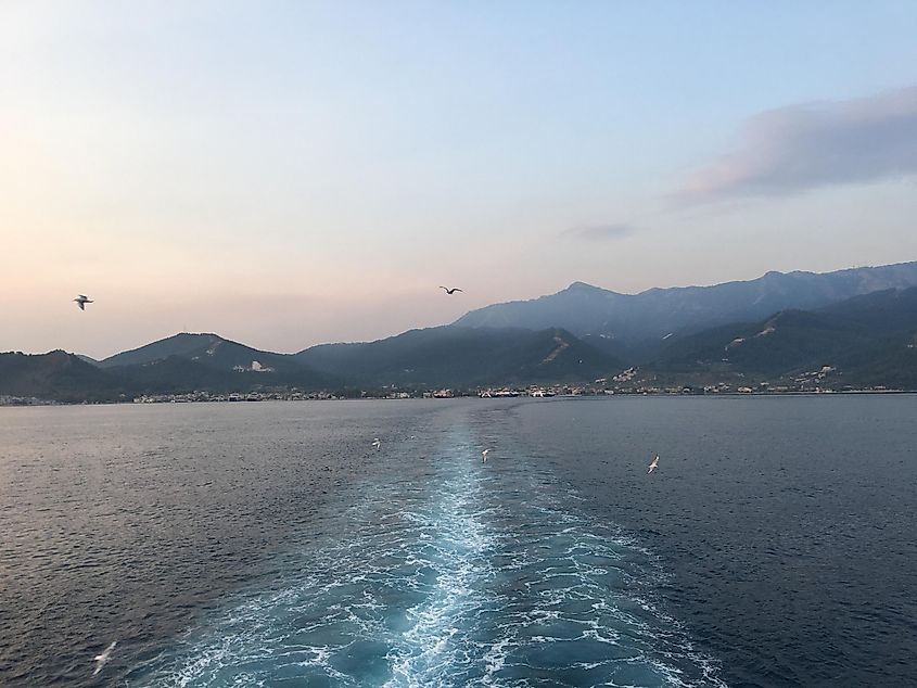 The wake from a ferry can be seen marking a watery trail from a mountainous island. It is an early, and beautiful morning. 