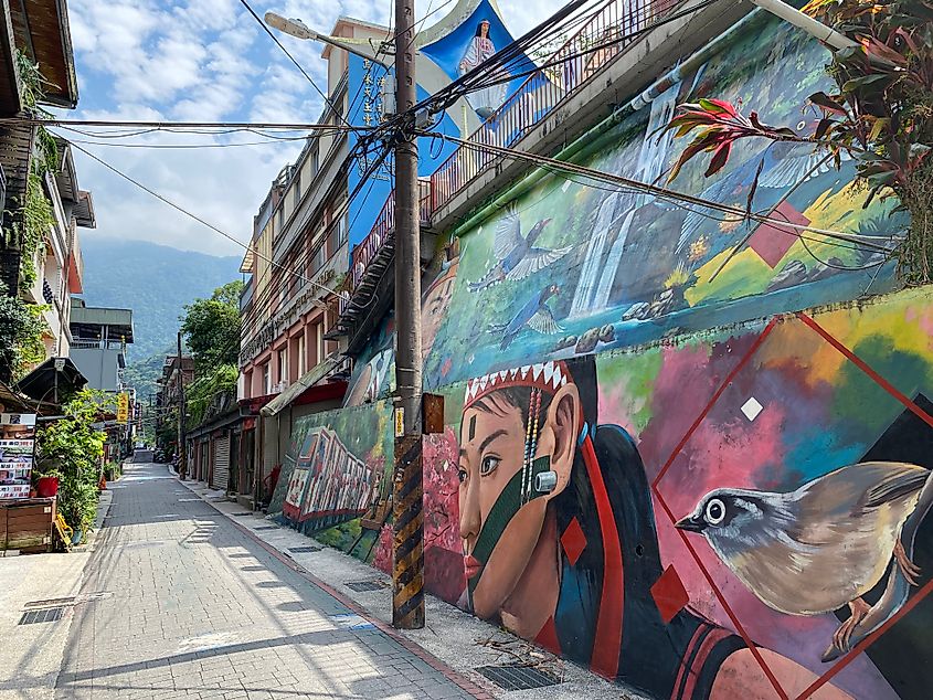 A colorful street mural showing Indigenous people, animals, waterfalls, and a train.