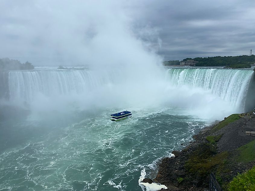 A blue tour boat approaches the base of a massive, curved waterfall.