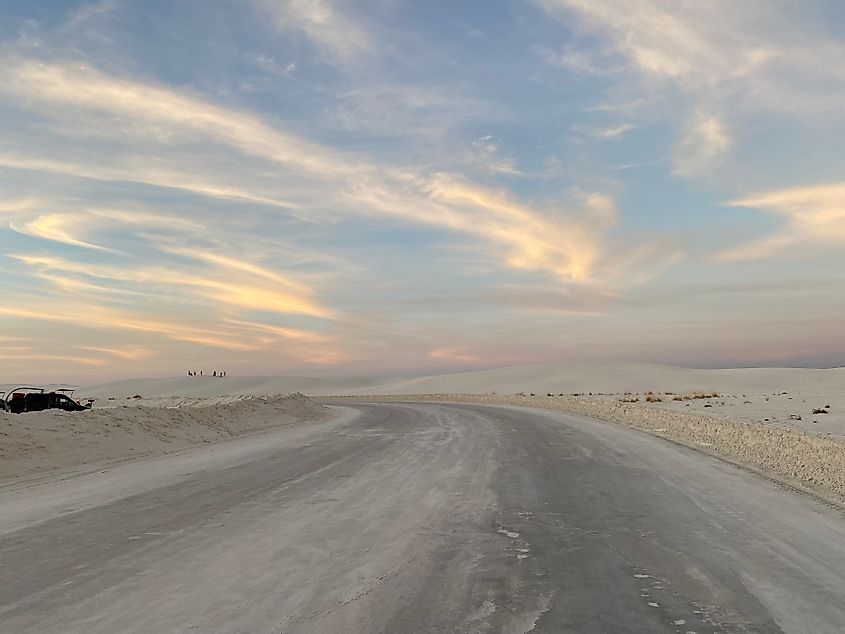 A basic road cuts through white dune fields underneath a pastel sky.