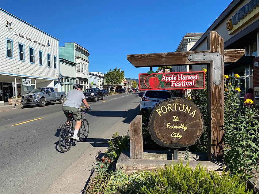 A man bikes past Fortuna's wooden welcome sign citing the Apple Harvest Festival and the nickname "The Friendly City"