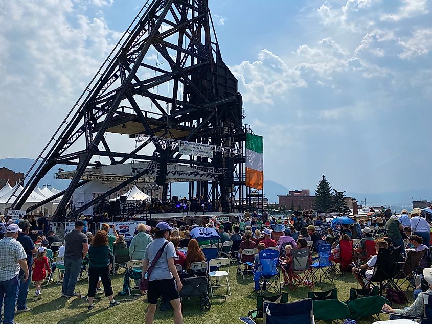 Traditional Irish dancers perform on a stage beneath an old oil rig to a crowd full of people.