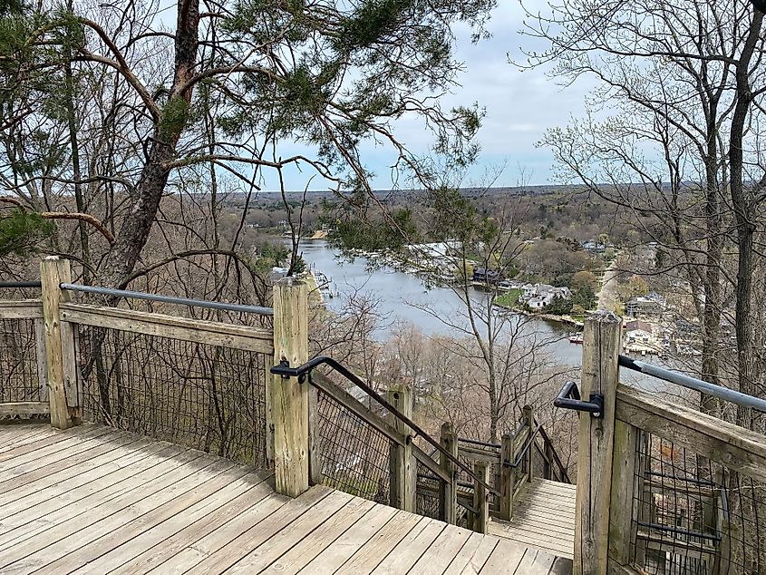A wooden staircase leads down through the forest and toward a small river town.
