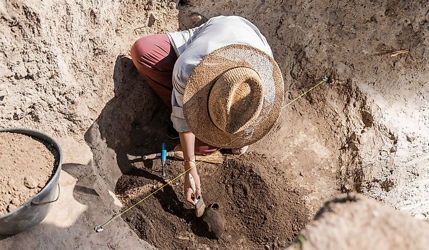 Female archaeologist digging up ancient pottery object at an archaeological site