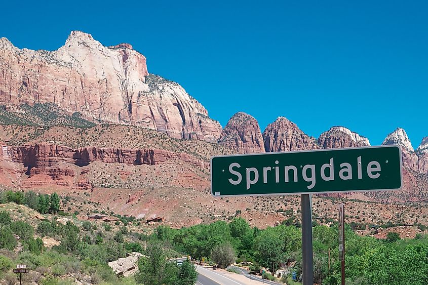 Sign for Springdale against a backdrop of striking red rock formations and clear blue sky in a desert landscape, evoking a sense of adventure.