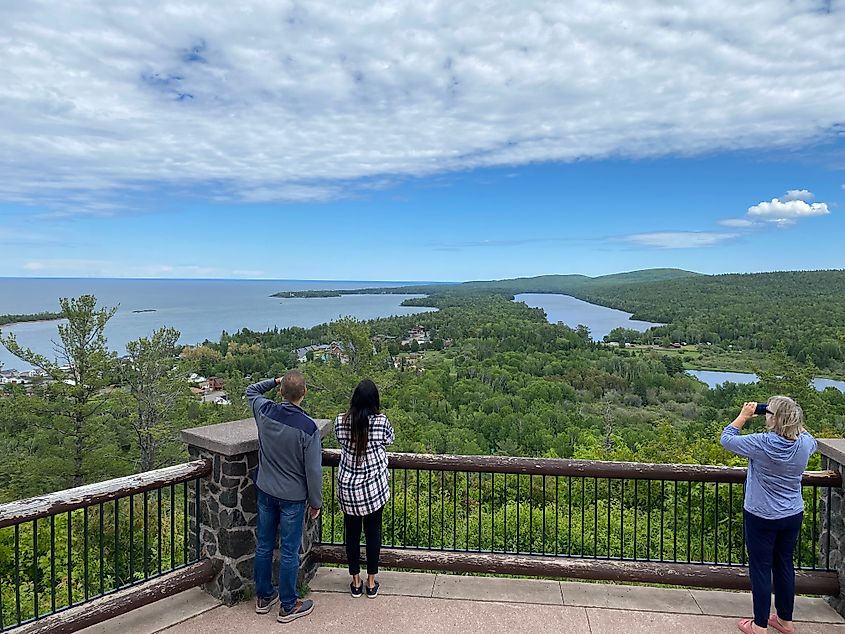 Three people standing atop a viewpoint platform, admiring the forest and Lake Superior scenery below.