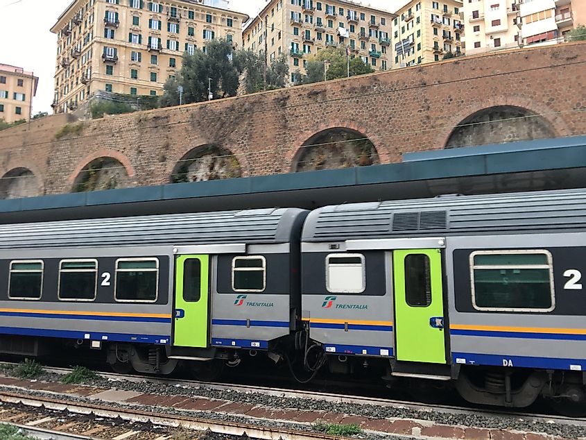 An Italian train with bright green doors waits in a station with large brick arches. 