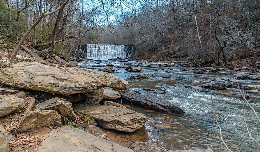 Standing downstream looking at the waterfall spilling into the creek at the old mill park in Roswell Georgia on a sunny day in winter