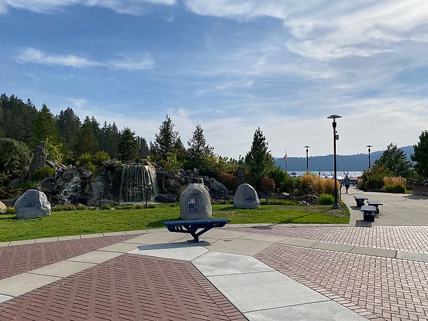 A waterfall memorial stands before a forested mountain and lakefront. 