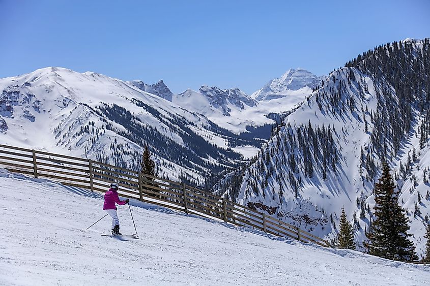 A woman downhill skier with the Maroon Bells and Colorado Rocky Mountains in the background in winter