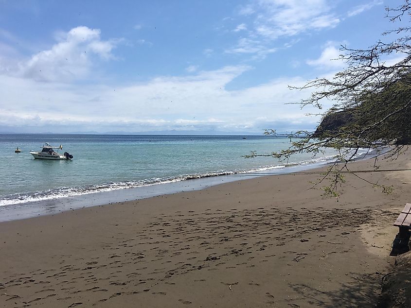 A boat sits anchored just off shore from a sandy island beach