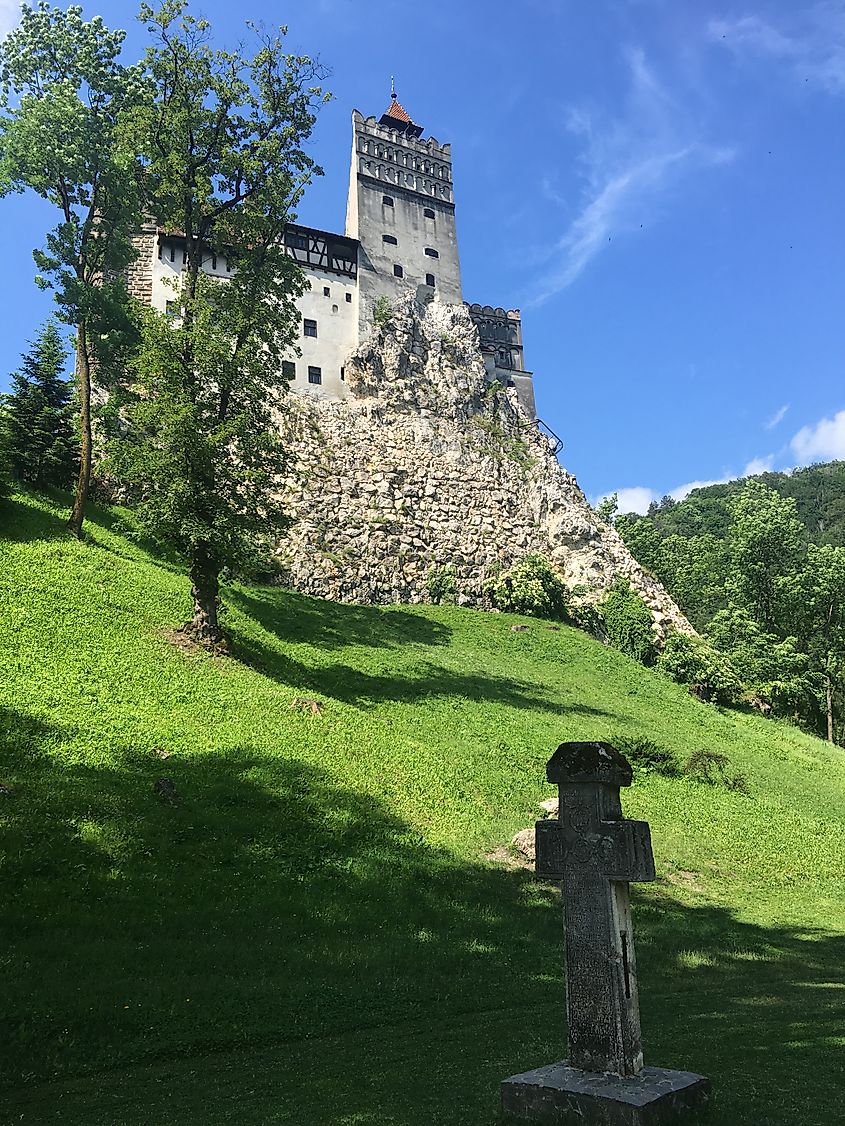 A slim, ominous looking castle with an old stone cross in the field before it. 