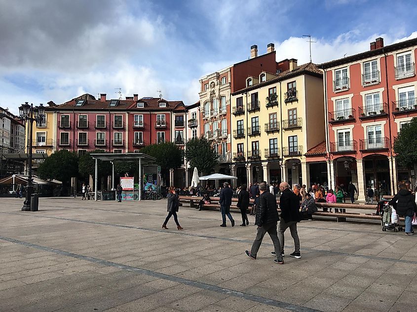 People walk jovially through a colorful town square, specifically, Plaza Mayor in Burgos, Spain.