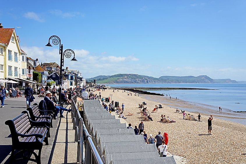 Tourists relaxing on the beach and promenade with views along the coastline, Lyme Regis, Dorset, UK