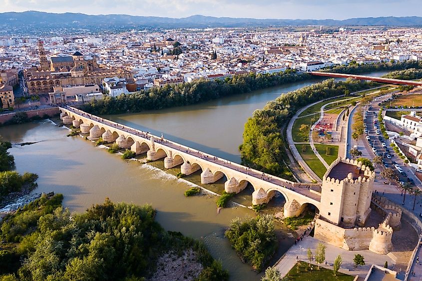 Scenic aerial view of ancient Roman bridge across Guadalquivir river and Moorish architecture of Mezquita-Catedral on background with Cordoba cityscape, Spain