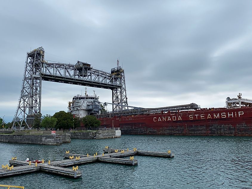 A lake freighter passes beneath a steel lift bridge into a narrow canal.
