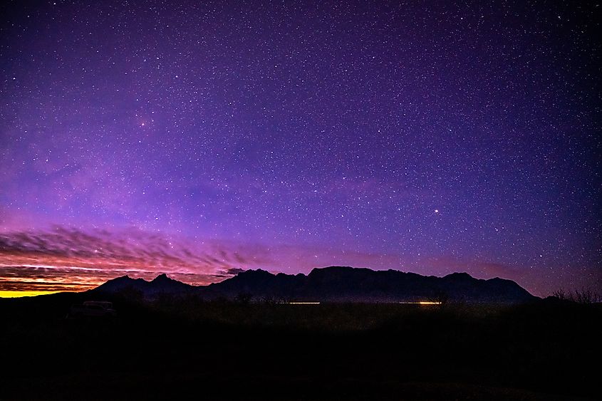 Sunlight and Car Lights Below Night Sky and Chisos Mountain Range in Big Bend National Park.