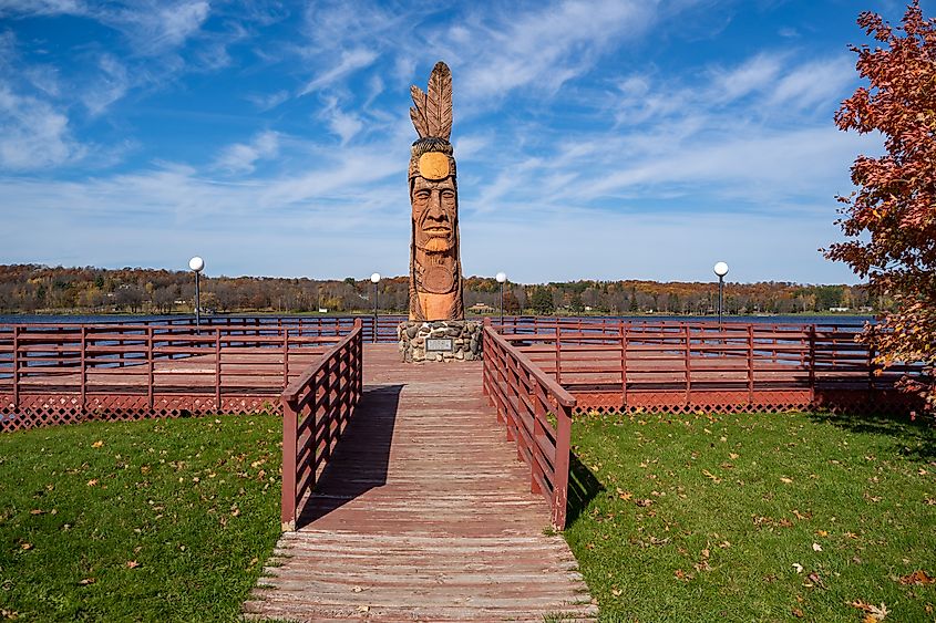 Editorial Photo Credit: melissamn via Shutterstock. Wakefield, Michigan - October 18, 2019: Trail of the Whispering Giants totem pole statue on Lake Superior by artist Peter Wolf