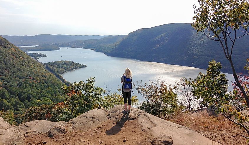 Young woman hiker standing and looking at river from the top of mountain