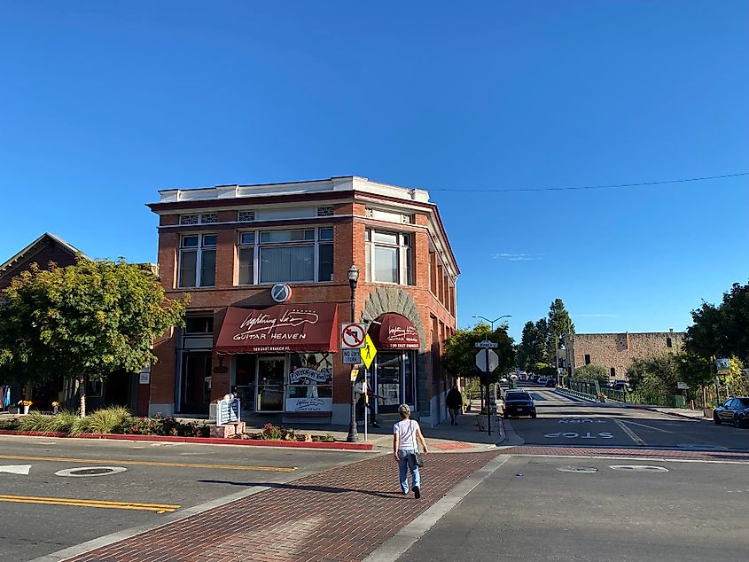 A woman crosses a quiet, small-town main street toward a large guitar shop.