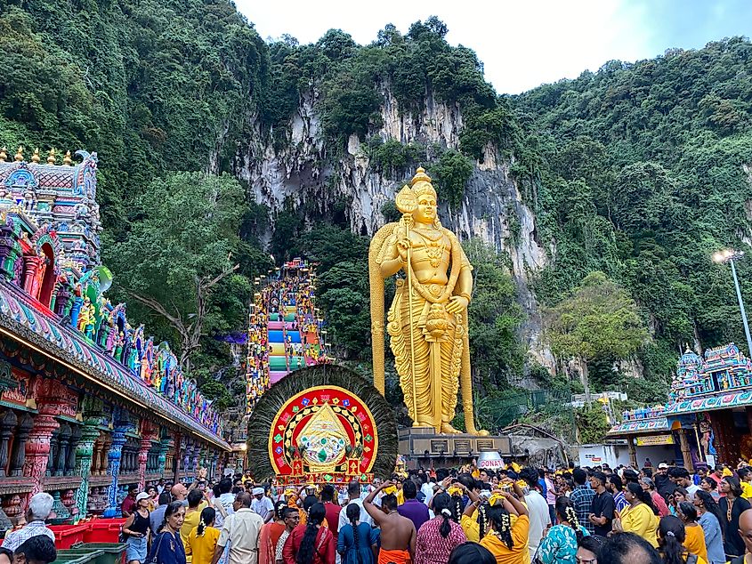 A large Hindu festival taking place beneath a tall golden statue and enormous rainbow staircase.