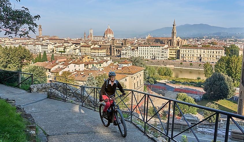 Cheerful senior woman cycling with her electric mountain bike above downtown of Florence with stunning view over the old city, Tuscany, Italy