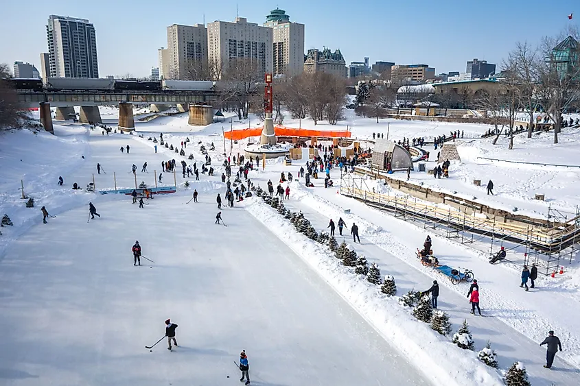 People skating at the Red River Mutual Skate Trail and playing hockey at an outdoor rink at The Forks on a sunny winter afternoon.