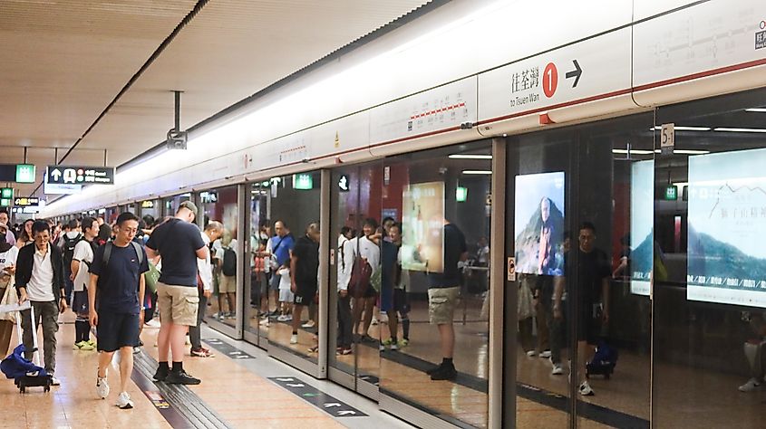 MTR train platform with glass door and some passengers waiting.