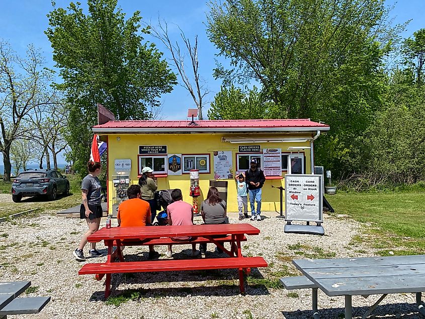 A small crowd queues outside of a yellow ice cream and hot dog stand.