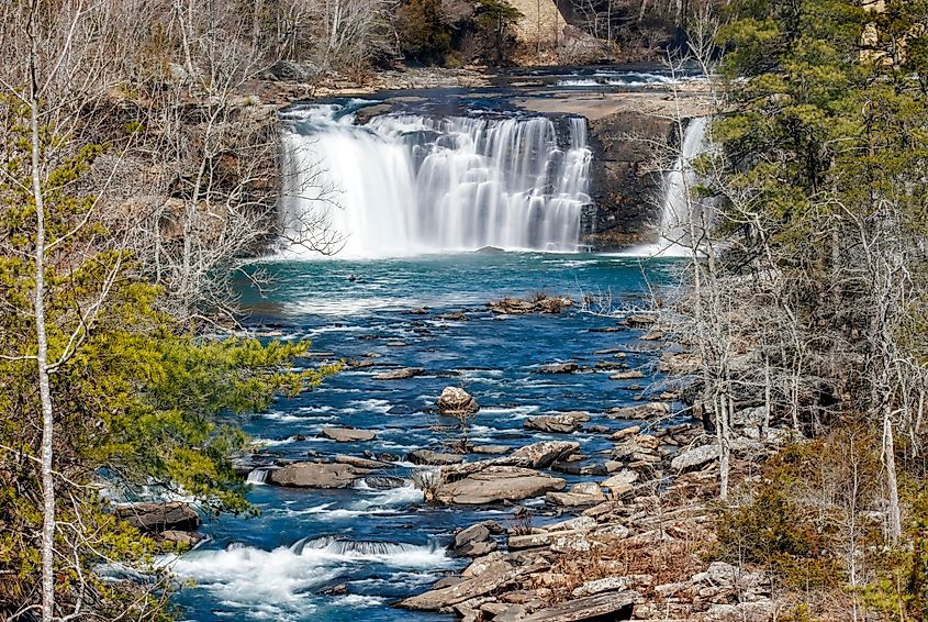 A wide waterfall cascades into a blue pool surrounded by trees.