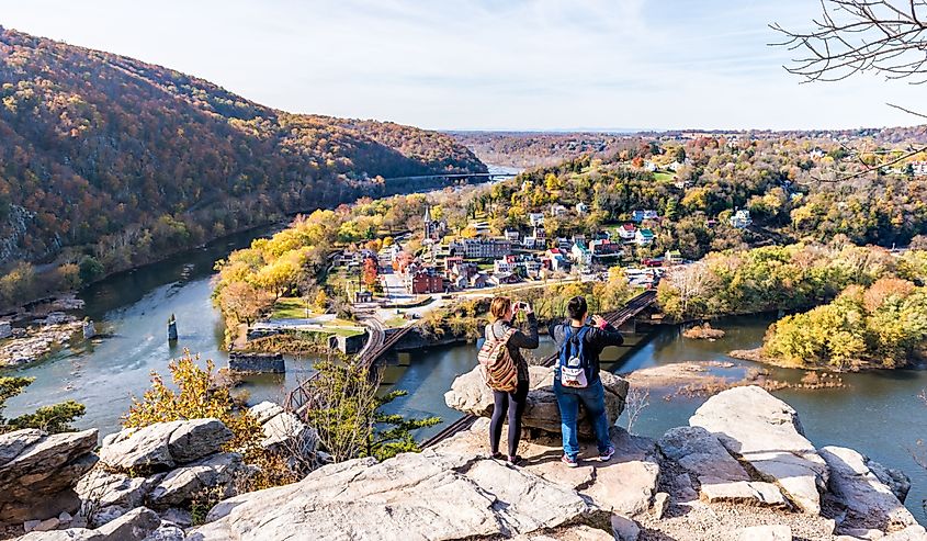 Overlook with hiker people women couple, colorful orange yellow foliage fall autumn forest with small village town by river in West Virginia, WV