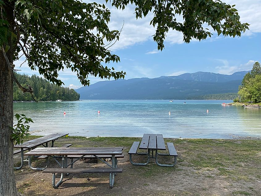 A cluster of picnic tables before the mountainous glacial lake at Whitefish Lake State Park.