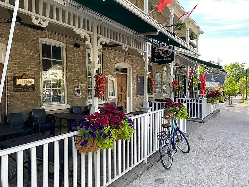 A bicycle leaned up against a white fence outside of an old fashioned brick hotel.
