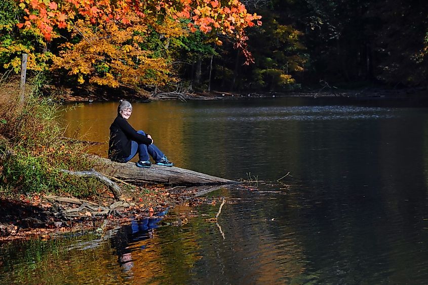 Female visitor smiles, she is sitting quietly on a log besides PoplarTree Lake in Meeman-Shelby State Park near Memphis, Tennessee.