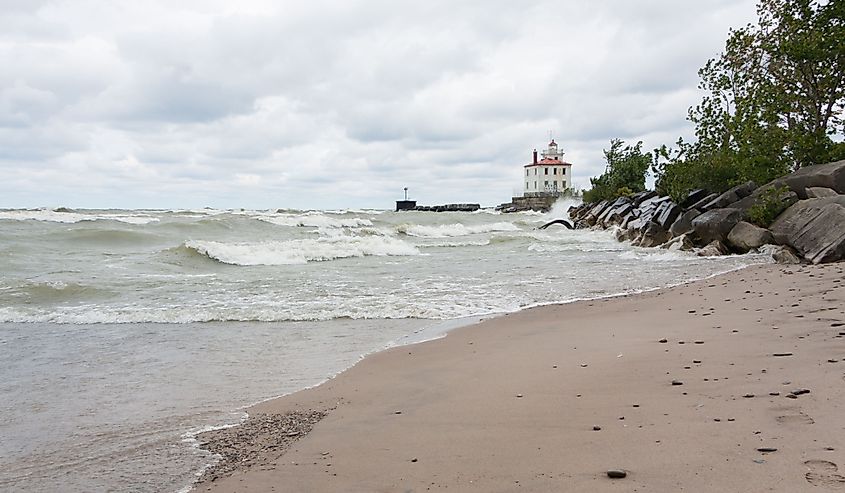 Lighthouse at Mentor Headlands Beach State Park in Ohio with waves crashing on shore and dark clouds overhead.