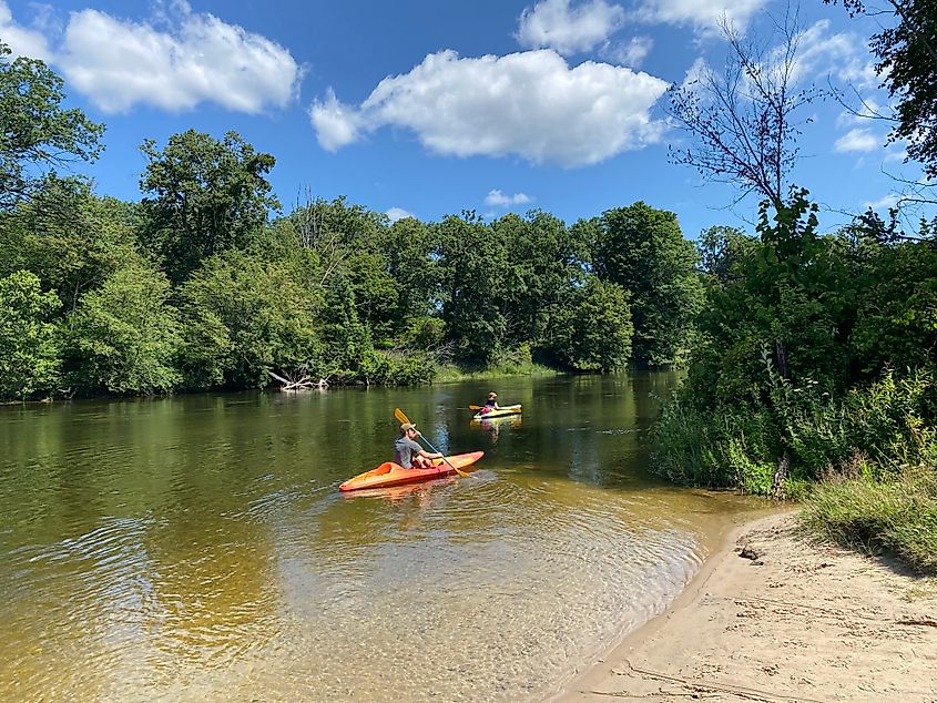 Two kayakers begin their paddle along a forest lined river.