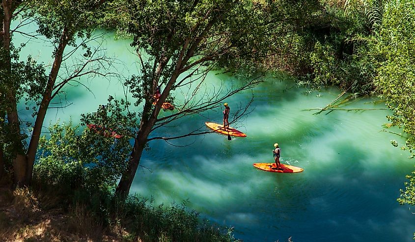 A group of people playing on orange kayaks over a blue river in the forest along the Jucar River in Spain