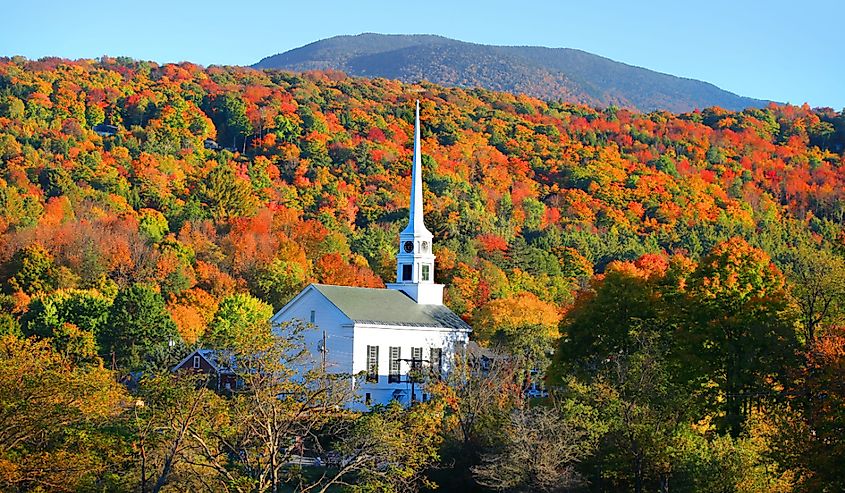 Iconic church in Stowe, Vermont with vibrant fall colors surrounding the town.