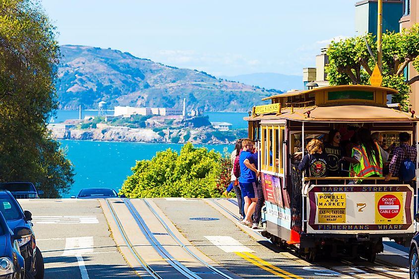 Alcatraz Island and cable car full of tourist passengers at crest of Hyde Street on sunny day