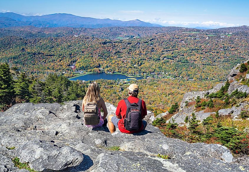 People sitting on a cliff edge enjoying scenic view. Couple on hiking trip relaxing and looking at beautiful autumn mountain scenery. Grandfather Mountain State Park, Banner Elk, North Carolina, USA.