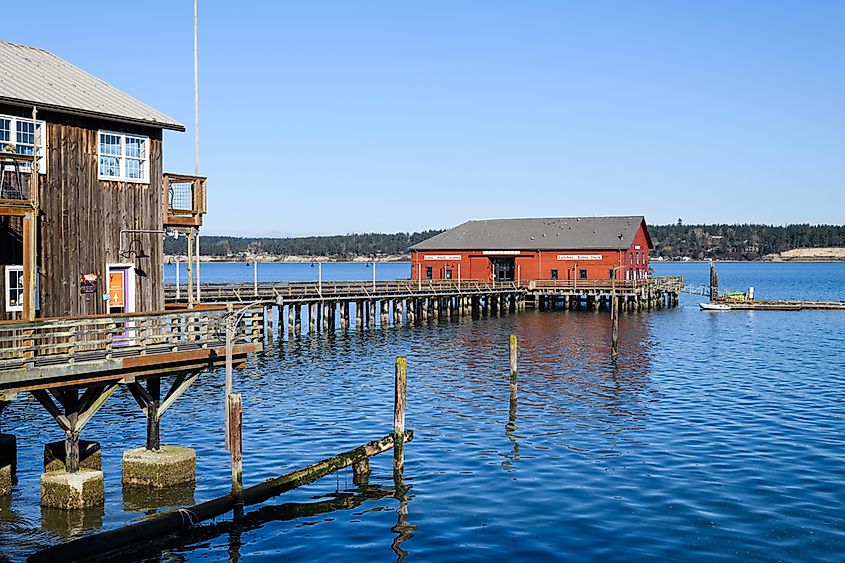 Red wooden building on the Coupeville Wharf in Washington State under clear blue sky with view of Penn Cove, via Ian Dewar Photography / Shutterstock.com
