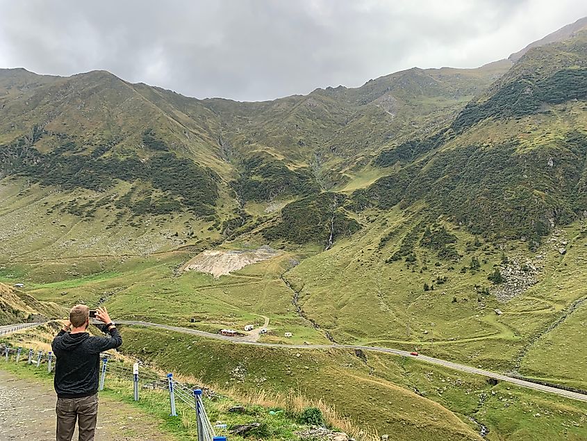 A man takes a picture of a winding mountain road.