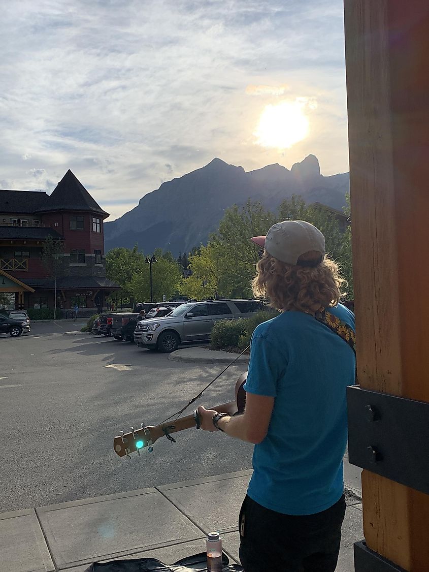 A man playing guitar in a parking lot as the sun sets over beautiful mountains. 