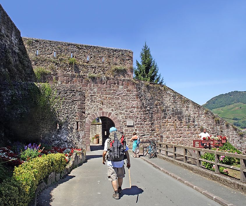A backpacker walks underneath a stone wall tunnel/gate. 