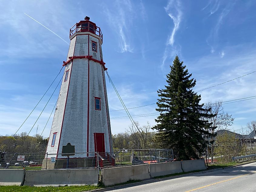 A weathered white and red lighthouse partitioned off and supported with guy lines.
