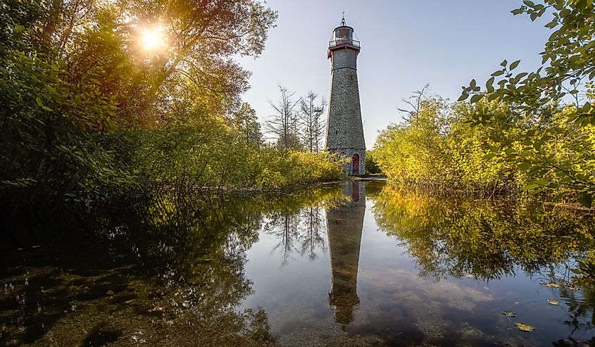 Beautiful golden light shining on a stone lighthouse, reflecting in water surrounding by lush green trees at Gibraltar Point Lighthouse, Toronto Islands.