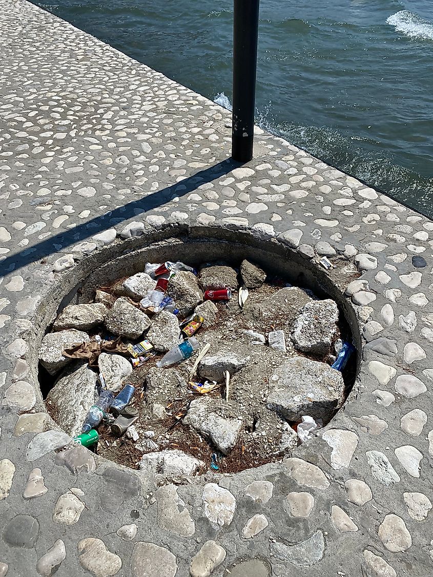A hole in a seaside sidewalk filled with garbage and broken rocks.